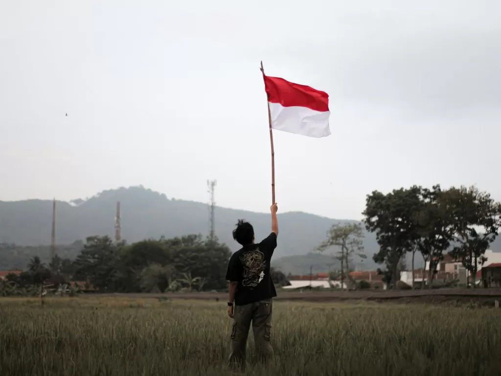 a man holding a red and white flag in a field