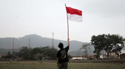 a man holding a red and white flag in a field