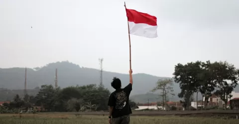 a man holding a red and white flag in a field